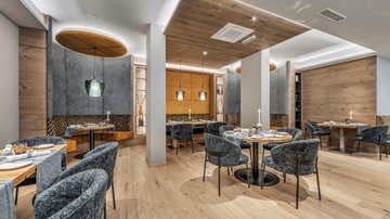 A modern restaurant with stylish round tables and comfortable chairs. The walls are painted in neutral tones, complemented by appealing lighting elements.