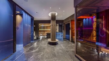 An elegant wellness area with modern saunas and a stylish reception area. The floor is made of dark marble and the walls shine in soft colors.
