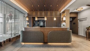 An elegant reception with stylish wood design and modern lamps. In the background, large windows with curtains can be seen, creating a bright atmosphere.