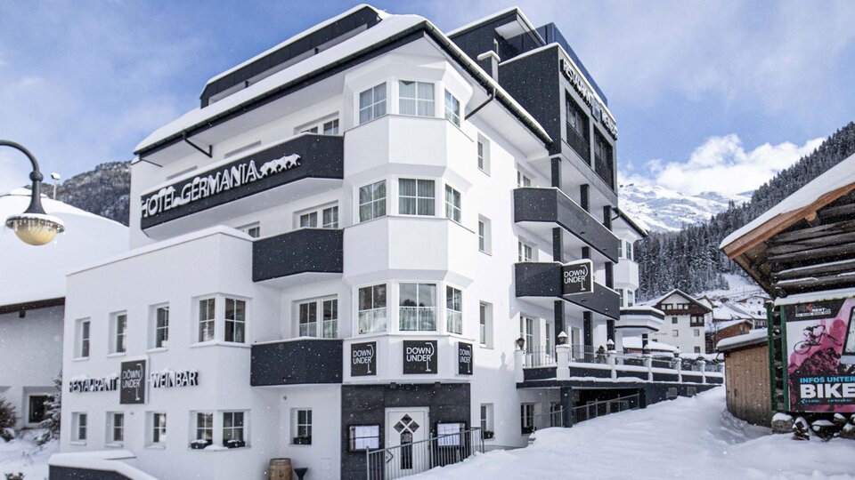 A modern hotel building in the snow with clean lines and large windows. The surroundings are characterized by snow-covered mountains.