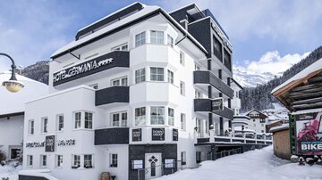 A modern hotel building in the snow with clean lines and large windows. The surroundings are characterized by snow-covered mountains.