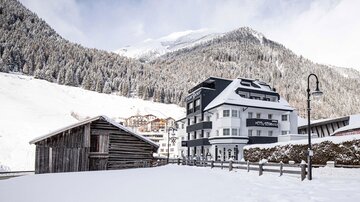 A charming hotel in a wintry landscape with snow-covered mountains. In the foreground stands a rustic wooden building.