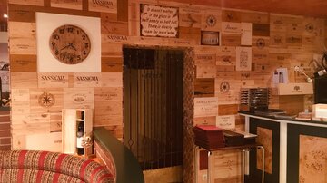 A cozy restaurant wall decorated with wooden boxes and various decorations. On the left side, there is a clock and an entrance to the background.