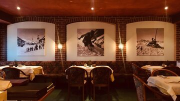 A cozy restaurant with a warm atmosphere. Historical black-and-white photos of winter sports activities hang on the walls.