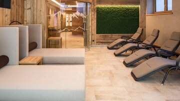 A modern wellness area with comfortable loungers and a cozy atmosphere. The walls are made of wood and there is a green plant wall.