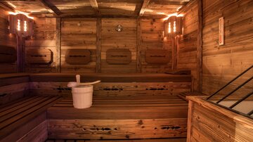 A sauna with wooden walls and benches. In the middle stands a wooden bucket.
