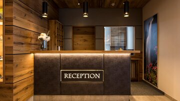 A modern hotel reception with wooden paneling and elegant lamps. The reception desk is well-lit and attractively designed.