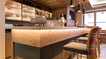 A stylish bar with wooden details and elegant chairs. Bottles and glasses are clearly visible in the background.