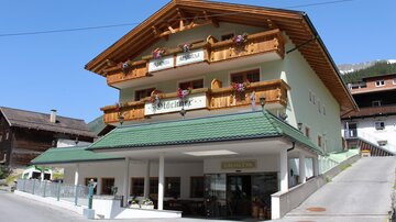 A cozy house with a traditional alpine style. The façade is adorned with blooming flowers and wooden elements.