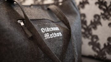 An elegant black felt bag with the inscription "Glöckner Marthon". The background features a patterned cushion.