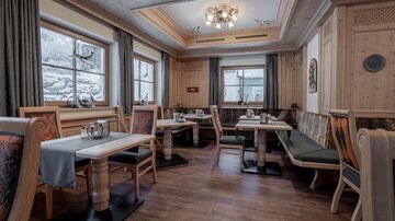 A cozy restaurant with wooden decor and tables. Large windows offer a view of the nature outside.