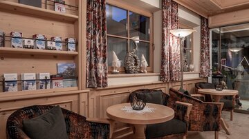 A cozy seating area with two chairs and a wooden table. The walls are made of wood with decorative curtains and windows that let in a lot of light.
