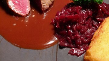 A plate with pink roasted meat, surrounded by a brown sauce. Served with broccoli, red beets, and potato dumplings.