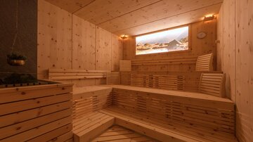 A modern sauna with wooden elements and several benches. A window overlooking a landscape creates a relaxing atmosphere.