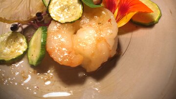 An elegant dish with shrimp, zucchini, and lime slices. Decorated with edible flowers, served on a gray plate.