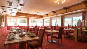 A cozy restaurant with red upholstered furniture and set tables. Large windows let in plenty of daylight.