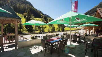 A cozy terrace with tables and parasols. In the background, a picturesque mountain landscape stretches out.