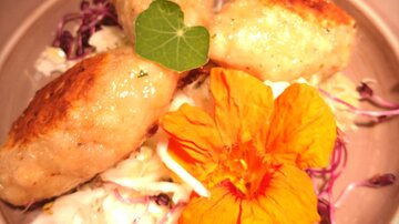 A plate with three golden-brown fried dumplings, surrounded by fresh sauerkraut and edible flowers. The dish is attractively decorated and looks appetizing.