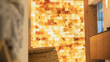 A modern designed room with a glowing salt stone wall. In the foreground, there is a basket and some decorative elements.