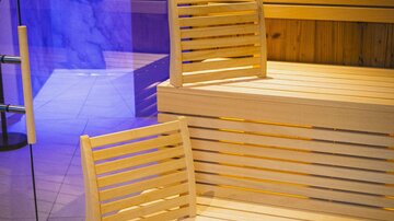 A modern sauna with bright wooden benches and relaxing lighting. The area looks clean and inviting.