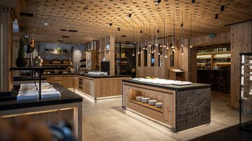 A modern restaurant with wood interiors and elegant lighting fixtures. The decor is stylish and inviting, ideal for cozy meals.