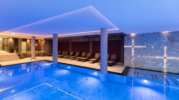 A modern wellness area with a blue pool and comfortable loungers. The lighting creates a relaxing atmosphere.