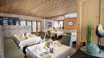 An elegant restaurant with beautifully set tables and a cozy ambiance. The wooden elements and the softness of the colors create an inviting atmosphere.