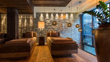 A modern spa with cozy loungers and warm light. The walls are made of stone and large windows provide a view outside.