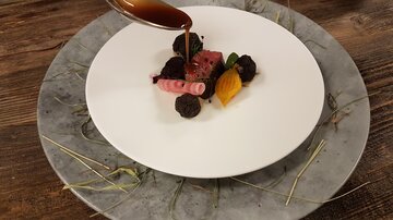 An elegant dish on a white plate, garnished with colorful vegetables and sauces. The plate is presented on a rustic wooden background.