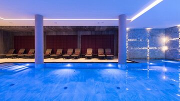 A modern wellness area with a clear blue pool and elegant loungers. Soft lighting creates a relaxing atmosphere.
