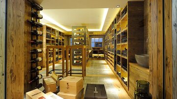 A stylish wine cellar with wooden shelves showcasing various wines. Boxes and bottles are neatly arranged, creating an inviting atmosphere.
