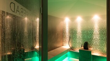 A relaxing steam room with soft green light and decorative walls. In the foreground, there is a resting spot with a figure.