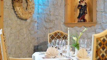 An elegantly set table in a cozy restaurant. Decorative elements hang on the stone wall in the background.