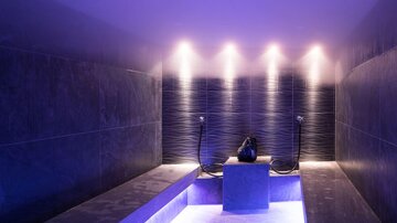 A modern wellness area with soft blue lighting and elegant stone surfaces. In the center, there is a stylish water basin.