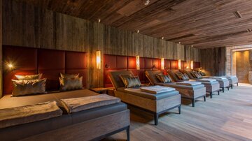 A luxurious relaxation room with several comfortable loungers and warm wood interior. Soft lighting creates a relaxing atmosphere.