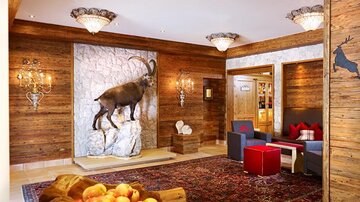 An inviting lobby with wooden walls and a large ibex on the wall. Stylish furniture and a carpet give the environment a cozy atmosphere.