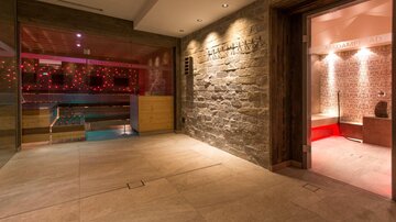 An elegant wellness area with a pool and atmospheric lighting. The room has a modern, calming atmosphere with stone walls and wooden details.