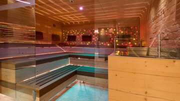 A modern wellness area with wooden paneling and colorful lights. The sauna is bright and invitingly designed.