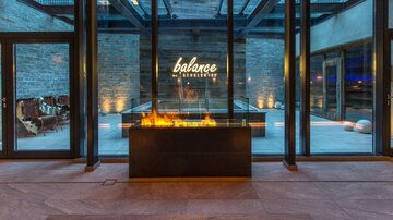 A modern reception area with large glass windows and an elegantly illuminated fireplace. The wall displays the logo "balance & co." in warm light.
