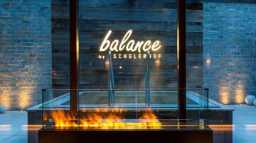 An elegant wellness area with a glass water basin and a stylish fire bowl. The inscription "balance" is prominently illuminated, creating a relaxing atmosphere.