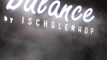 A creative neon sign with the inscription "balance by ISCHGLERHOF". The background is blurred, creating a relaxing atmosphere.