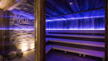 A modern sauna with a cozy atmosphere. Soft blue lighting and wooden surfaces create a relaxing environment.
