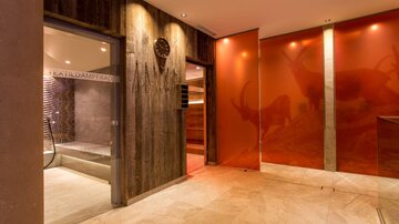 An elegant wellness area with warm wood tones and soft lighting. On the left side, there is access to various relaxation areas.