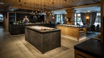 A modern restaurant with wood and stone decor. In the foreground is a large counter with fresh food and a chef.
