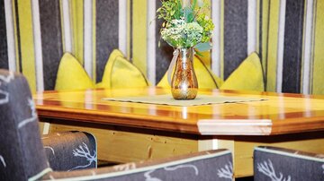 A cozy table with a floral vase amidst comfortable chairs and cushions. The walls are decorated with striped fabric in shades of yellow and gray.