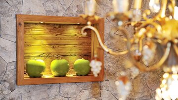 A decorative box with three green apples on a wooden wall. In the background, a crystal chandelier can be seen.