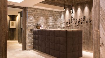 An elegant reception area with a padded reception desk and a stone wall. The warm lighting creates an inviting atmosphere.
