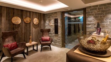 An elegant reception area with modern armchairs and rustic stone masonry. The warm colors and decorative elements create a pleasant atmosphere.