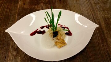 An artfully arranged dish on a white plate. It contains fish, rice, herbs, and a fruity sauce.
