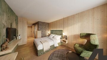 A modern hotel room with wooden paneling and a large double bed. A stylish corner with a green armchair and a television complements the space.